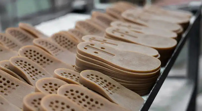 Des rangées de semelles de chaussures beiges avec des trous de ventilation disposées en motif.